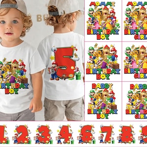 Peut inclure: T-shirts blancs avec des graphiques colorés représentant des personnages de jeux vidéo. Un t-shirt dit "BIRTHDAY BOY" et l'autre a un grand chiffre rouge 5 au dos. D'autres motifs incluent "MOMMY", "DADDY" et les chiffres 1 à 9.
