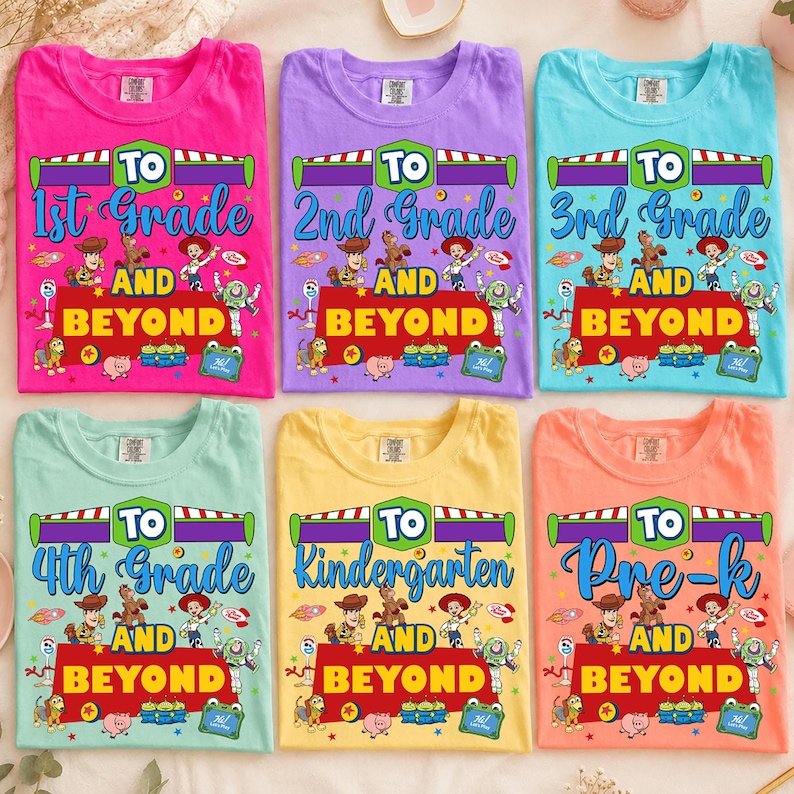 May include: A collection of six colorful t-shirts in pink, purple, light blue, mint green, yellow, and orange. Each shirt features a graphic print with the text 'TO [Grade] AND BEYOND' and various cartoon characters from the Toy Story film franchise.
