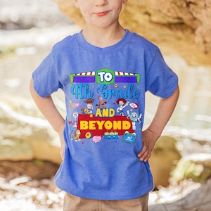 May include: A blue short-sleeved t-shirt featuring a graphic print with the text TO 4th Grade AND BEYOND. The design includes colorful illustrations of various animated toy characters, including a cowboy, a cowgirl, a space ranger, and others.