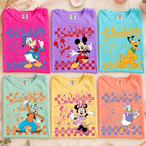 May include: Six crew neck t-shirts in bright colors, each featuring a Disney character: Donald Duck on pink, Mickey Mouse on purple, Pluto on light blue, Goofy on mint green, Minnie Mouse on yellow, and Daisy Duck on peach, all with 1928 text.