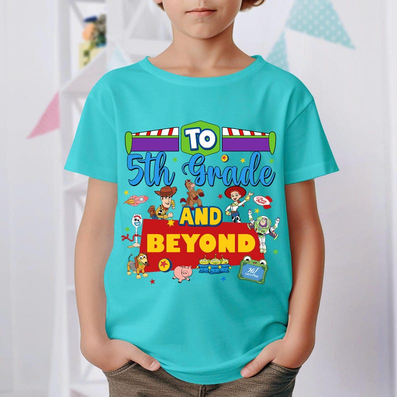 May include: A bright turquoise short-sleeve t-shirt featuring a colorful graphic print with the text TO 5th Grade AND BEYOND. The design includes illustrations of various animated toy characters, including a cowboy, a space ranger, and aliens.
