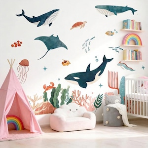 May include: A wall decal set featuring watercolour illustrations of marine life including whales, an orca, a stingray, a sea turtle, a jellyfish, a crab, and various fish, alongside coral reef elements, all arranged on a white wall in a room.