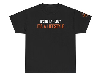 May include: A black short-sleeve t-shirt featuring the white text IT'S NOT A HOBBY and the orange text IT'S A LIFESTYLE centered on the chest. A small circular orange and black logo is visible on the right sleeve of the garment.