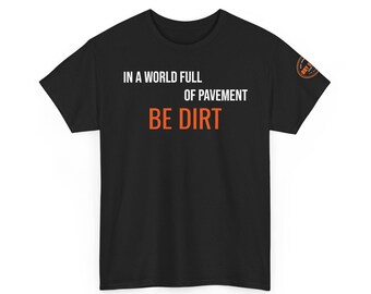May include: A black short-sleeve t-shirt featuring the white text "IN A WORLD FULL OF PAVEMENT" and the orange text "BE DIRT" on the front. A small circular orange and black logo is visible on the left sleeve area of the garment.