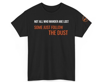 May include: A black short-sleeve t-shirt featuring the white text "NOT ALL WHO WANDER ARE LOST" and the orange text "SOME JUST FOLLOW THE DUST" on the front. A small circular orange and black logo is visible on the left sleeve of the garment.