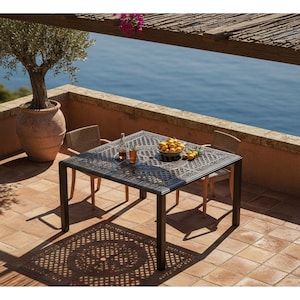 May include: An outdoor patio scene with a dark metal table and two chairs. A bowl of lemons sits on the table, along with two glasses and a bottle. A large terracotta pot with a tree is in the background, with a view of the ocean.