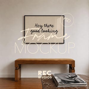 May include: A rectangular black frame containing a beige print with the black text Hey there good looking. The frame is mounted on a plain wall above a wooden bench with a brown seat and a stack of magazines on a marble table in the foreground.