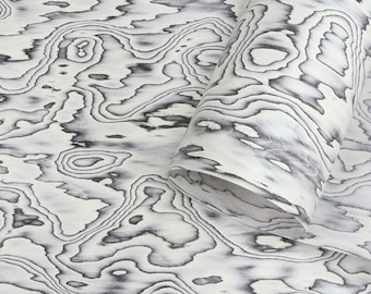 May include: A roll of decorative paper with a distinctive wood grain design. The pattern showcases swirling grey and black lines on a white backdrop, producing a marbled appearance. The paper is partially rolled, displaying the pattern.