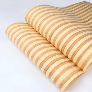 May include: A flexible sheet of material featuring a repeating pattern of alternating light beige and medium brown vertical stripes. The surface has a smooth, wood-like grain texture and is curved into two overlapping, wave-like rolls.
