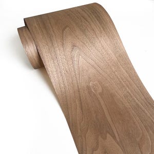 Può includere: Un rotolo di impiallacciatura in legno marrone con motivi di venature visibili. L'impiallacciatura è di colore marrone chiaro e sembra flessibile. Il legno viene probabilmente utilizzato per la fabbricazione di mobili o altri progetti di falegnameria.