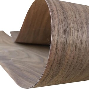 Könnte beinhalten: Ein flexibles Blatt aus Holzfurnier in hellbrauner Farbe mit sichtbarer Maserung. Das Material ist über sich selbst gebogen und zeigt eine glatte Oberflächenstruktur sowie ein dünnes Profil, das die natürliche Holzoptik unterstreicht.