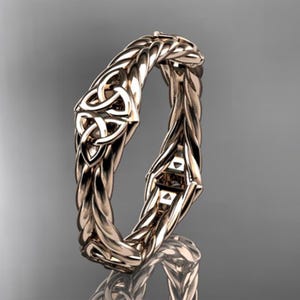 May include: A bronze-colored ring with a Celtic knot design. The ring features a braided band and a prominent Celtic knot at the top. The ring is displayed against a gray background.