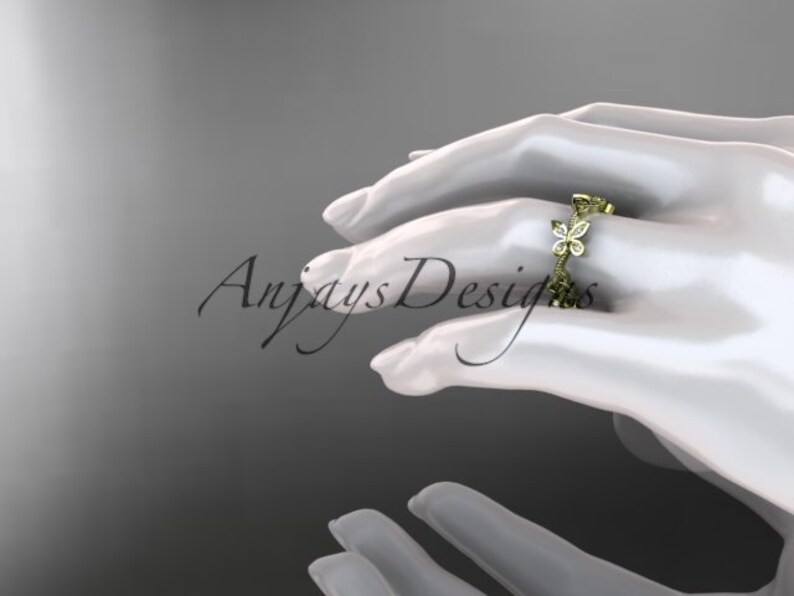 Puede incluir: Un anillo de banda de oro con un delicado dise&ntilde;o de mariposa engastado con peque&ntilde;os diamantes. El anillo est&aacute; en la mano de una modelo.