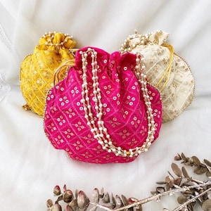 May include: Three drawstring pouches in bright pink, yellow, and cream, each featuring a diamond-patterned fabric with small metallic sequins. The pink pouch is centred and adorned with a long, multi-strand white pearl bead handle.