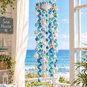 May include: A hanging mobile featuring a circular wooden frame with cascading spiral crochet ribbons in shades of blue, white, and teal. The mobile is adorned with various seashells, starfish, and small beads, creating a coastal-themed decoration.