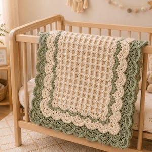 May include: A rectangular crochet blanket featuring a cream-colored waffle stitch center. The blanket is bordered by a wide, scalloped edge in alternating layers of cream and sage green yarn, creating a textured, layered appearance.