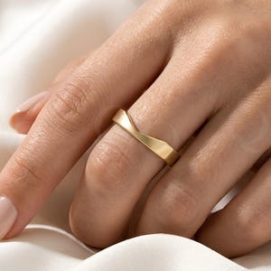 Peut inclure: Une bague en or avec une finition mate lisse et un sommet en forme de V distinct. L'anneau présente une largeur uniforme et un design angulaire épuré qui se place au centre du doigt, mettant en valeur une teinte dorée jaune métallique.