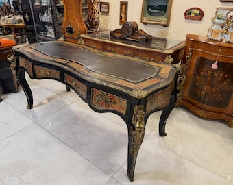 May include: An antique black desk with a dark leather top and ornate gold accents. The desk features curved legs and decorative trim with floral and geometric patterns. A classic piece of furniture.
