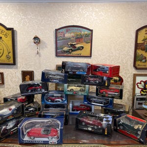 Könnte beinhalten: Eine Sammlung von Modellautos in Schachteln, darunter Jaguar, Porsche und Mercedes-Benz. Die Autos sind in verschiedenen Farben erhältlich, darunter Rot, Silber und Schwarz. Einige Schachteln tragen Aufschriften wie "METAL" und "CLASSICO".