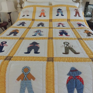 May include: A white and yellow quilt with a patchwork design featuring appliqued figures of people wearing overalls. The quilt is made with a variety of fabrics, including denim, plaid, and solid colors.