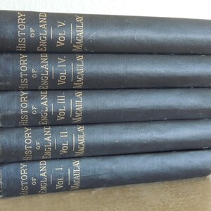 May include: A stack of five vintage books with dark gray covers. The spines display gold lettering that reads "History of England" and the author's name, Macaulay. The volumes are labeled I through V.