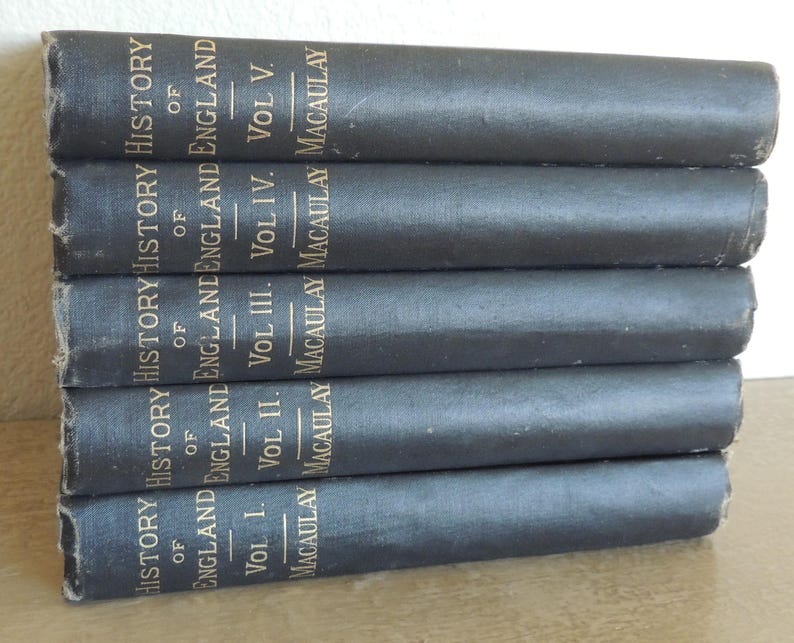 May include: A stack of five vintage books with dark gray covers. The spines display gold lettering that reads "History of England" and the author's name, Macaulay. The volumes are labeled I through V.