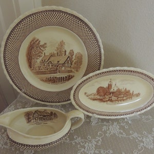 May include: Set of three vintage ceramic plates featuring brown and white illustrations of historic buildings. The plates have a brown lattice border. The plates feature the text "The Homestead Village", "The Franciscan Monastery", and "Sharon's Croft".