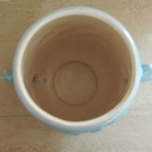 May include: A light blue ceramic planter with two handles. The planter is empty and has a smooth, glazed finish.