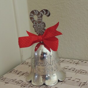 May include: Silver Christmas bell with a red bow and a candy cane ornament. The bell is inscribed with "Christmas 1993".