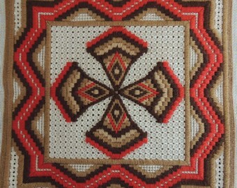 May include: A white fabric with a brown and red embroidered design. The design features a cross shape with four symmetrical patterns.