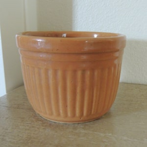 May include: A terracotta-colored ceramic planter with vertical ridges. The planter is empty and has a smooth, glazed finish.
