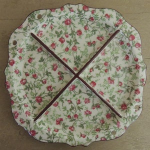 May include: A white ceramic divided serving dish with a floral pattern of red roses and green leaves. The dish has four sections separated by brown dividers.