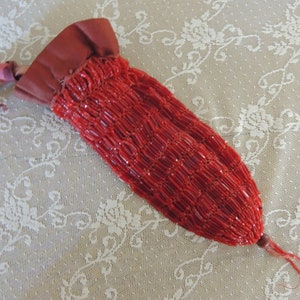 May include: A red beaded purse with a maroon fabric top and a drawstring closure. The purse has a long tassel.