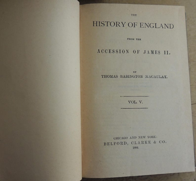 May include: Open book with text: "THE HISTORY OF ENGLAND FROM THE ACCESSION OF JAMES II. BY THOMAS BABINGTON MACAULAY. VOL V." Published by Belford, Clarke & Co. in Chicago and New York in 1884. The pages are off-white.