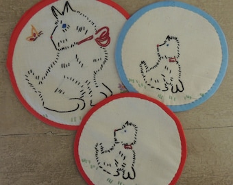May include: Three embroidered white cotton pot holders with red and blue trim. Each pot holder features a black embroidered image of a dog.