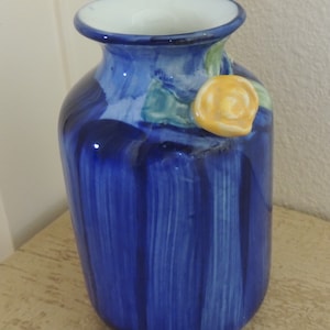 May include: A ceramic vase with a glossy, deep blue finish and a white interior. The vase features a hand-painted design with vertical brushstrokes and a yellow rose accent with green leaves. The vase is approximately 8 inches tall.