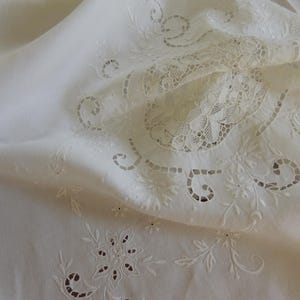 May include: A white fabric textile featuring intricate cutwork embroidery and lace inserts. The design displays floral motifs and scrolling patterns with delicate openwork details throughout the surface, creating a textured and layered appearance.