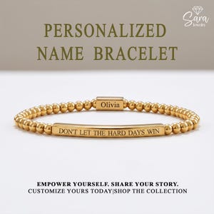 May include: A gold-toned beaded bracelet featuring a central rectangular bar engraved with the text DON'T LET THE HARD DAYS WIN and a smaller rectangular bead engraved with the name Olivia. The text PERSONALIZED NAME BRACELET is visible above.