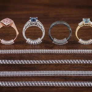 Könnte beinhalten: Vier Ringe mit verschiedenen Designs und Edelsteinen, darunter rosa, blaue und hellblaue Steine, werden gezeigt. Klare Ringgrößenversteller aus Kunststoff sind an den Ringen befestigt. Mehrere klare Ringgrößenversteller aus Kunststoff werden ebenfalls unter den Ringen angezeigt.