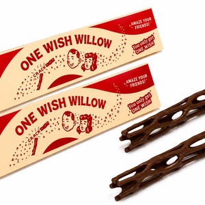 Puede incluir: Dos cajas triangulares de cartón con la etiqueta ONE WISH WILLOW en rojo y crema, con caras de dibujos animados y el texto AMAZE YOUR FRIENDS y You only get ONE WISH. Junto a las cajas hay dos palos cilíndricos de color marrón oscuro con un patrón de rejilla.