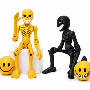 Puede incluir: Dos figuras de esqueleto articuladas, una amarilla y otra negra, cada una con una amplia sonrisa de dientes. El esqueleto amarillo está sentado, mientras que el negro está en cuclillas. Dos bolas amarillas con caras sonrientes los acompañan.