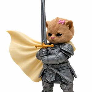 Op de afbeelding: Een beige kattenfiguur in gedetailleerd zilverkleurig harnas met fleur-de-lis accenten. De kat heeft een klein roze strikje op het hoofd en houdt een lang zilverkleurig zwaard met een gouden gevest vast. Een crèmekleurige cape wappert erachter.