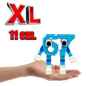 Può includere: Una figura blu pixelata con braccia e gambe, tenuta in una mano. La figura è alta 11 cm. La parola "XL" è visualizzata in rosso sopra la figura.