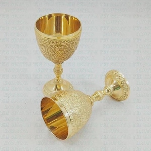 Pode incluir: Dois cálices de metal dourado com gravuras intrincadas de flores e vinhas no exterior das taças e nas bases. Um cálice está na vertical enquanto o outro está deitado de lado, ambos com um acabamento polido e brilhante e hastes ornamentadas.