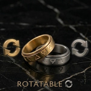 May include: Two metal rings, one gold and one silver, with geometric symbols engraved around the band. The word "ROTATABLE" is displayed in gold lettering below the rings. The rings are set against a dark, textured background.