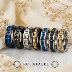 Könnte beinhalten: Eine Sammlung drehbarer Ringe in verschiedenen Farben, darunter Schwarz, Silber, Gold und Blau. Die Ringe haben ein einzigartiges Design mit einem rotierenden Mittelband. Das Wort "ROTATABLE" wird darunter angezeigt.