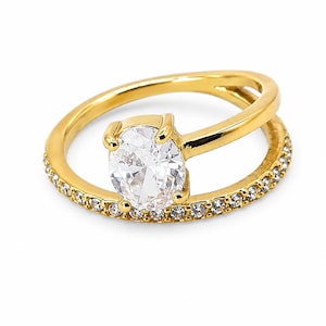 Peut inclure: Une bague dorée au design à tige fendue, ornée d'une pierre ovale transparente montée sur quatre griffes. L'anneau inférieur est incrusté d'une rangée de petites pierres rondes et transparentes sur la moitié avant de la bague.