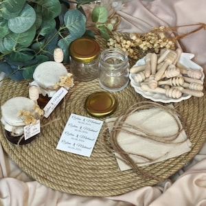Könnte beinhalten: Ein Set aus kleinen Glasgefäßen mit goldenen Deckeln, hölzernen Honiglöffeln, beigen Stoffquadraten und Bindfaden. Eine weiße Karte zeigt den aufgedruckten Text "Ozlem & Mahmut 06.06.2026", der viermal wiederholt wird.