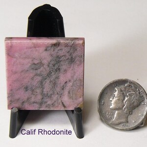 May include: A square, polished piece of pink and black California rhodonite stone displayed on a black plastic stand. Next to the stone is a silver-colored 1941 Mercury dime for scale. The text "Calif Rhodonite" is printed in purple below the stone.