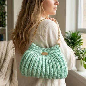 May include: A mint green, knitted handbag with a gold chain strap. The bag has a ribbed texture and a small, oval, brown leather tag. The bag is a shoulder bag style.